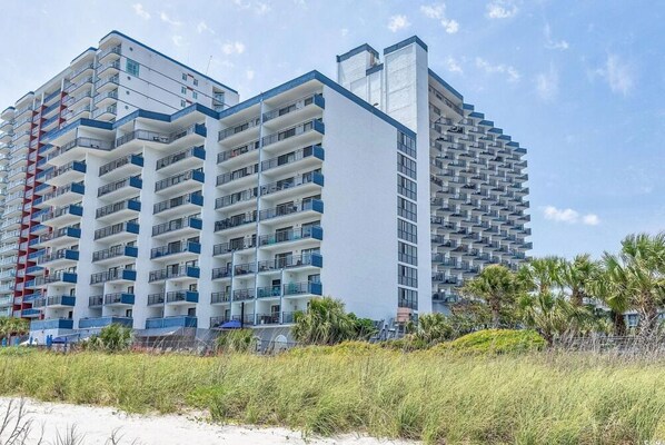 A high-rise hotel with multiple balconies, a flat roof, and a beach view.