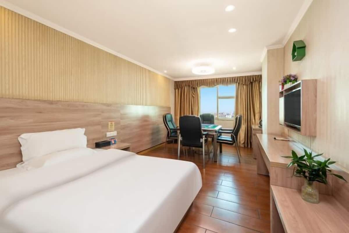 A hotel room with a large bed, a desk, a chair, a TV, and a window with curtains.