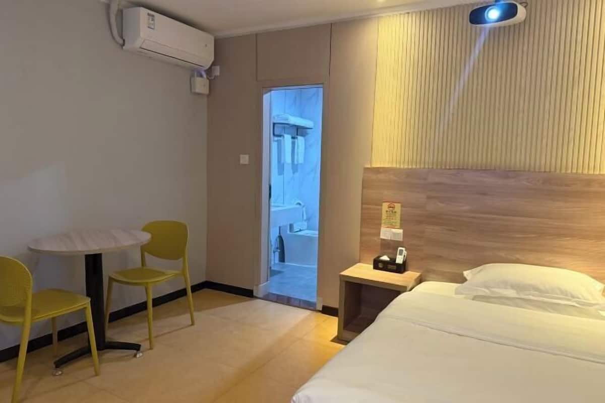 A hotel room with a bed, a small table with chairs, an air conditioning unit, and a wooden headboard.