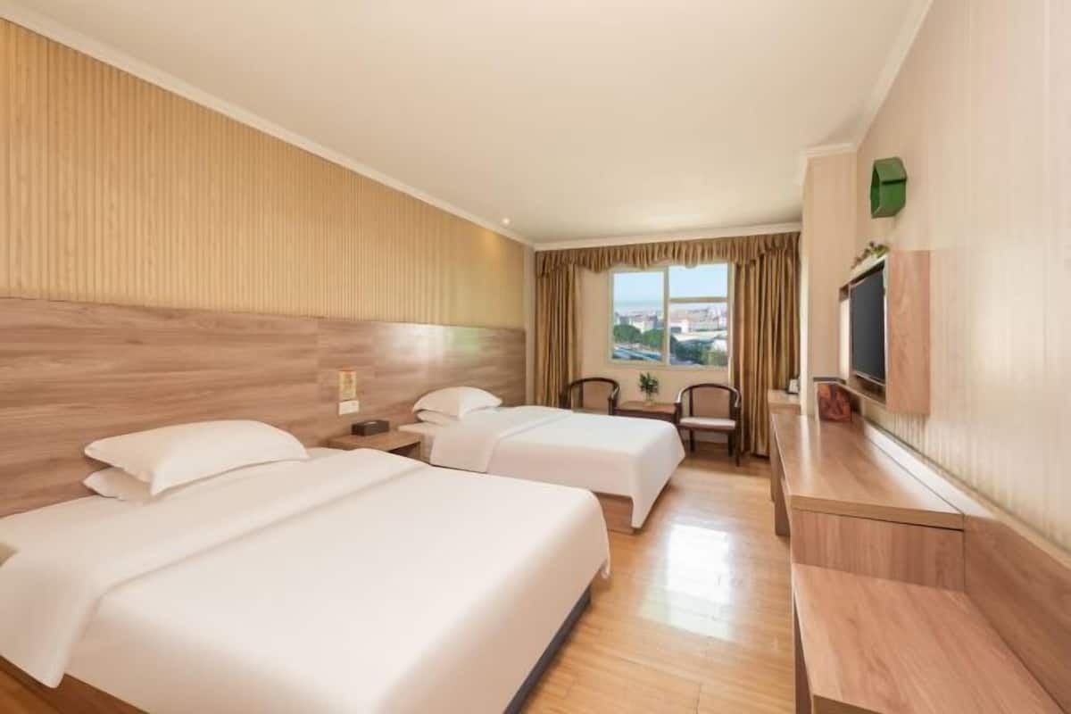 A hotel room with two beds, a desk, a chair, a TV, and a window with a view.