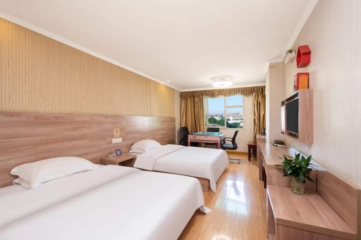 A hotel room with two beds, a desk, a chair, a TV, and a window with curtains.