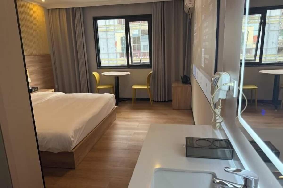 A hotel room with a bed, a small table, two chairs, a desk with a phone, and a window with curtains.