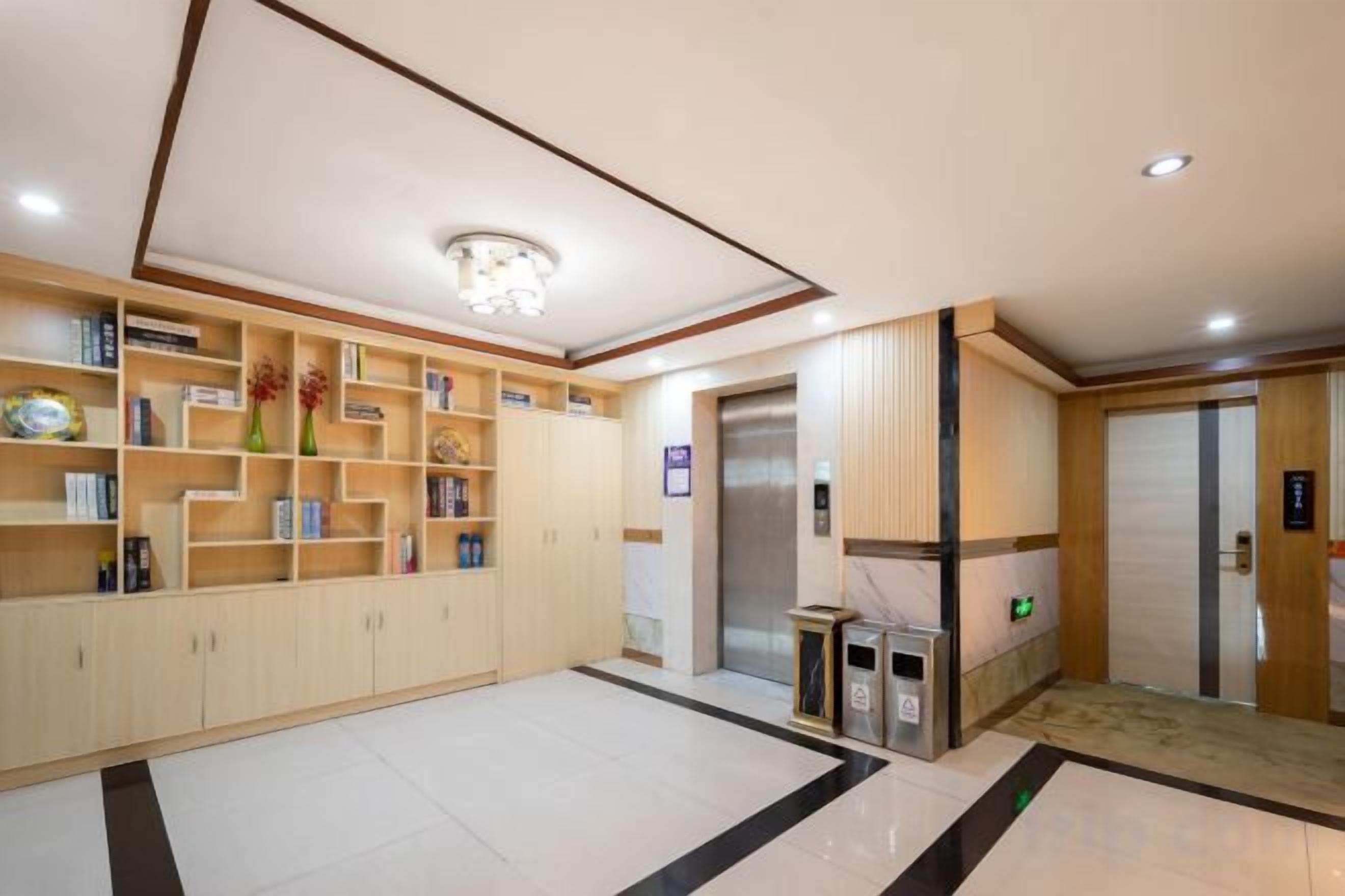Um saguão de hotel com balcão de recepção, estante de livros, elevador e lixeira.