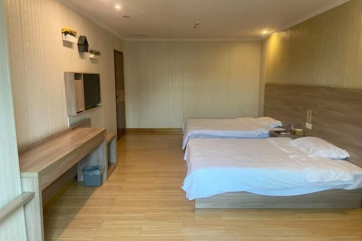 A hotel room with two beds, a bench, a TV, and a trash bin.