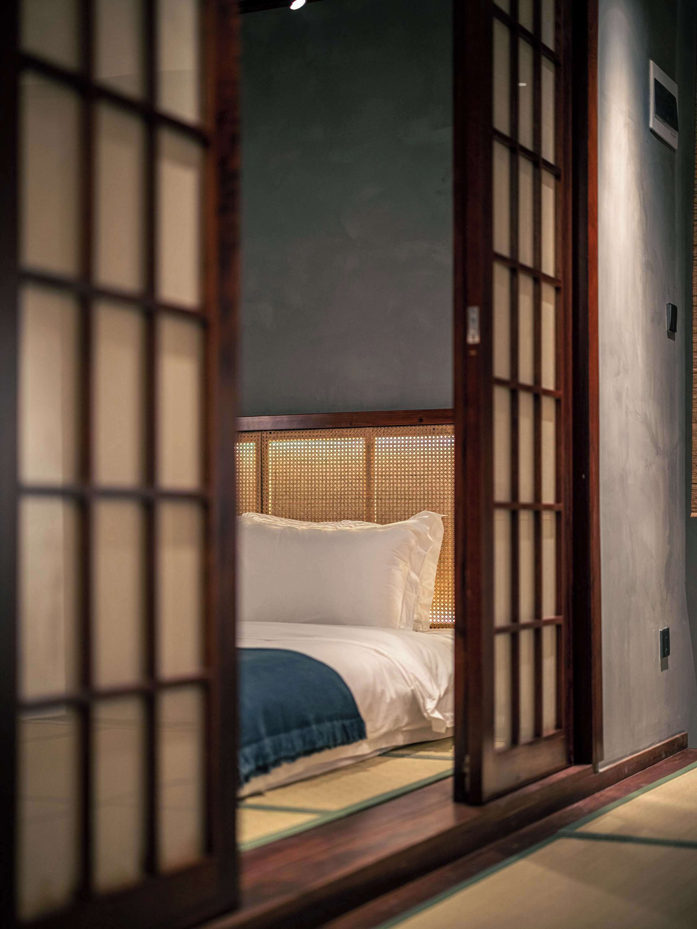 Une pièce de style japonais traditionnel, avec un sol recouvert de tatamis, un lit bas en bois avec une literie blanche et une porte coulissante en papier de riz (shoji).