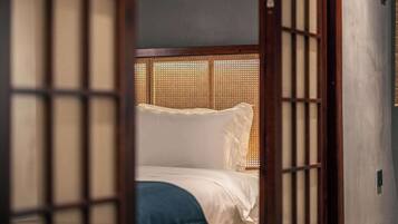 Une pièce de style japonais traditionnel, avec un sol recouvert de tatamis, un lit bas en bois avec une literie blanche et une porte coulissante en papier de riz (shoji).