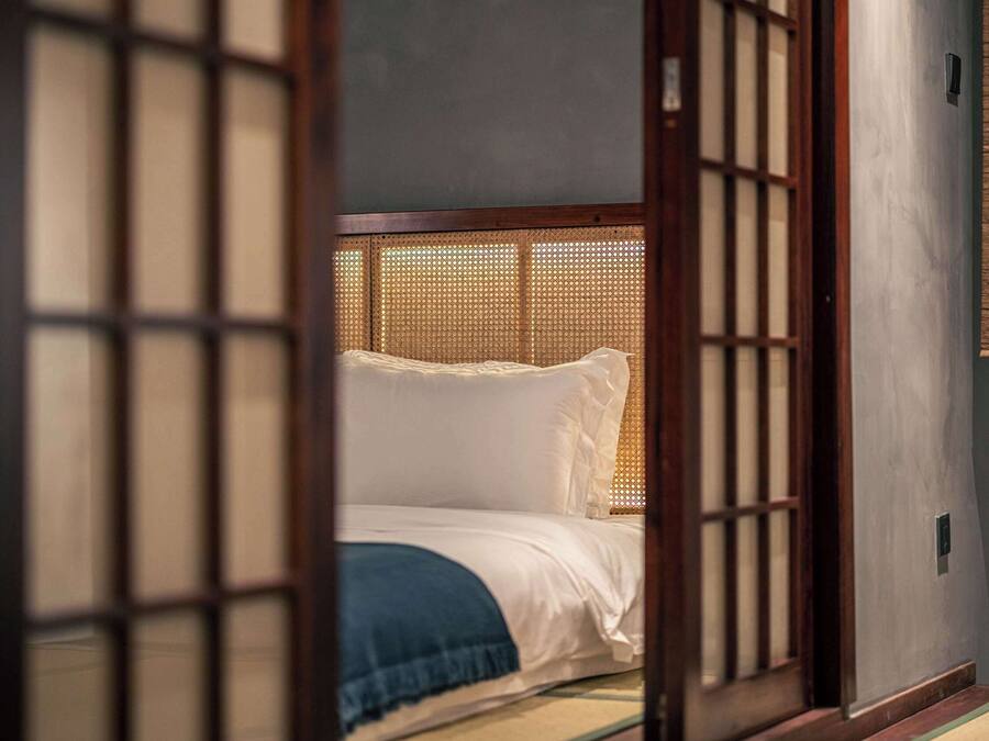 Une pièce de style japonais traditionnel, avec un sol recouvert de tatamis, un lit bas en bois avec une literie blanche et une porte coulissante en papier de riz (shoji).