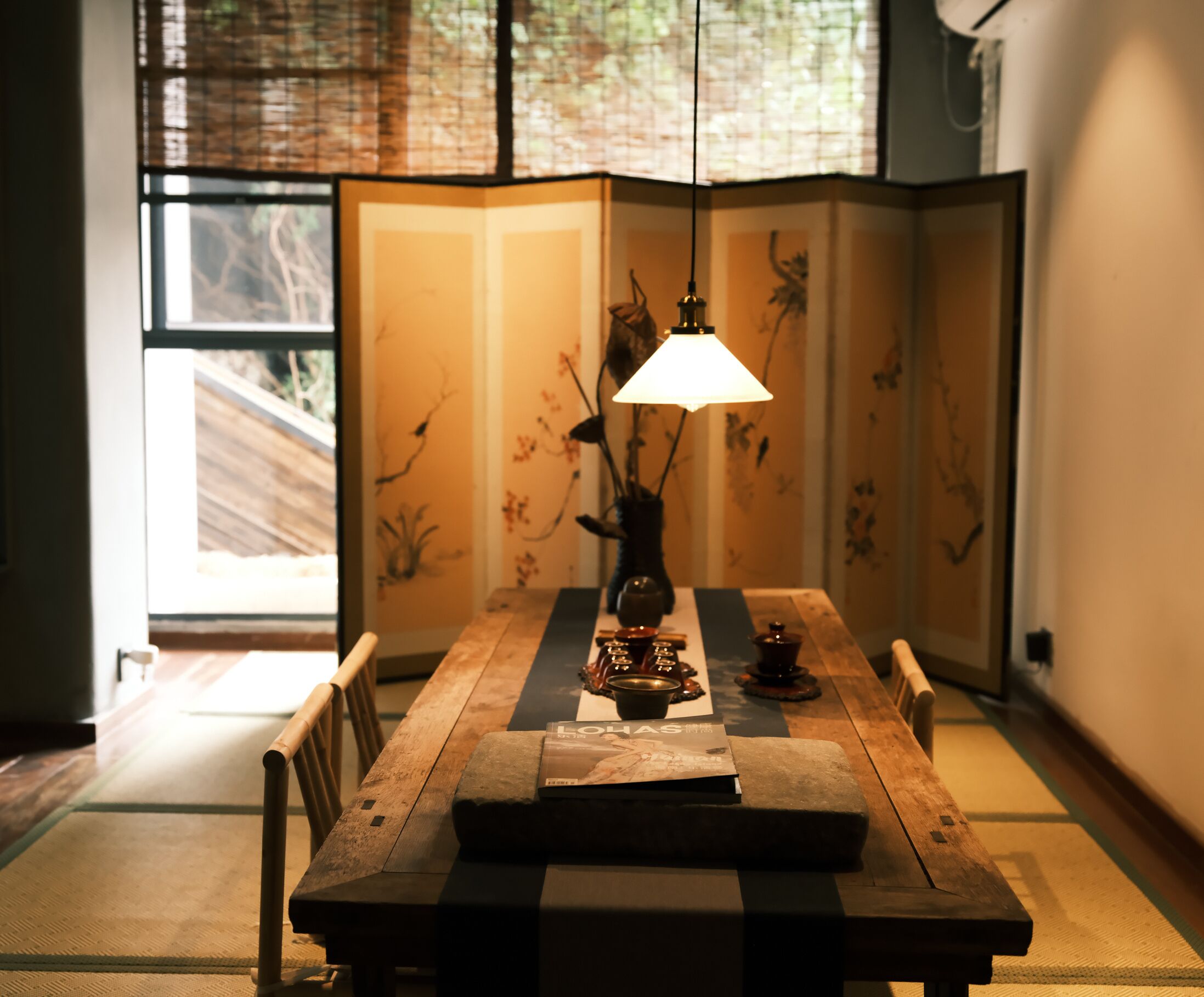 Una habitación japonesa tradicional con suelo de tatami, una mesa baja con una lámpara colgante y un shoji en el fondo.