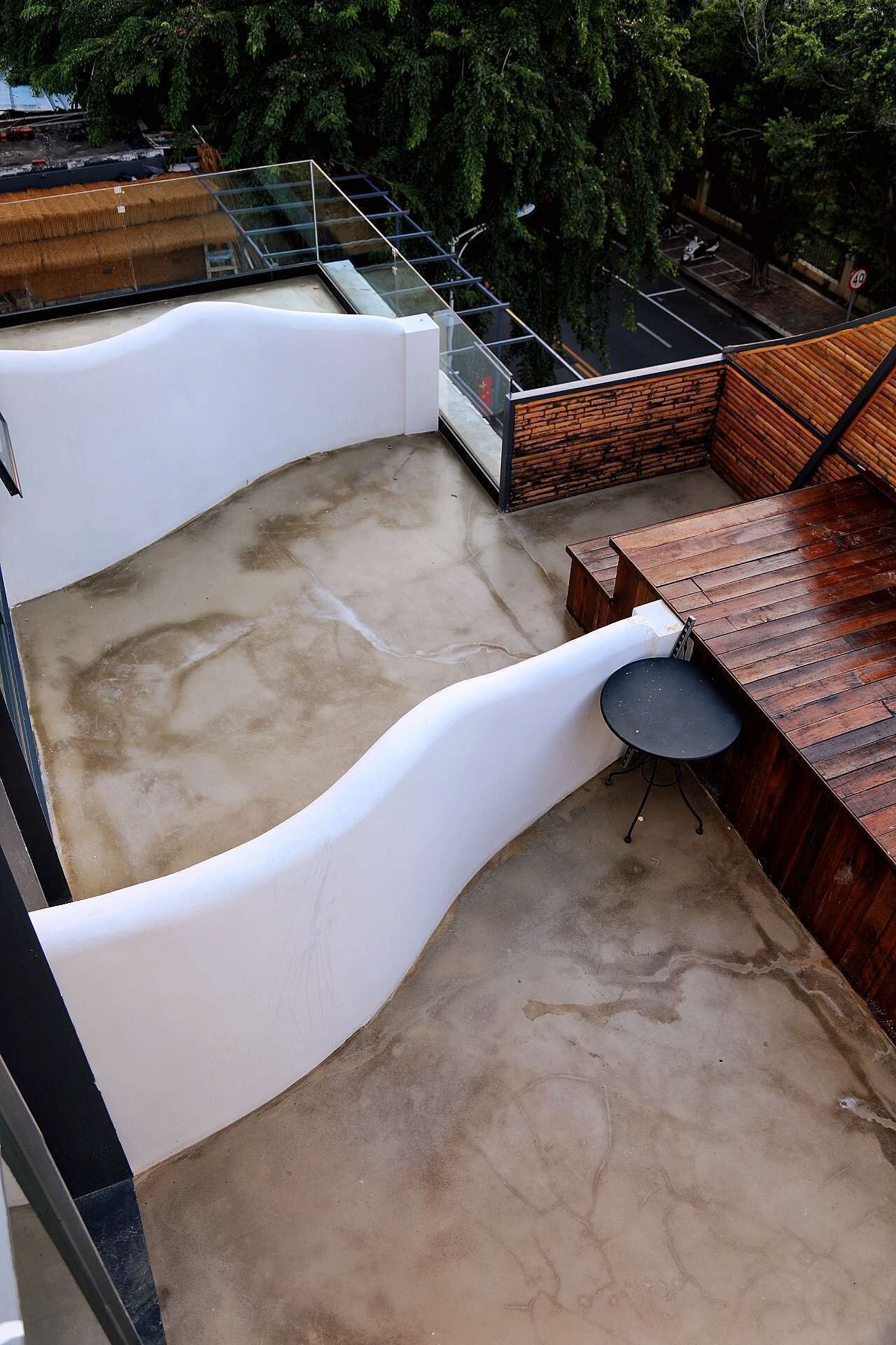 A rooftop terrace with a concrete floor, a wooden table, and a black chair.