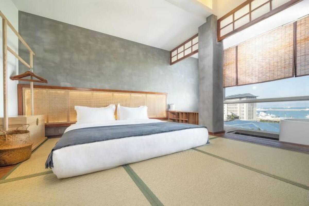 Ett modernt hotellrum med en stor säng, utsikt över staden och ett stort fönster.