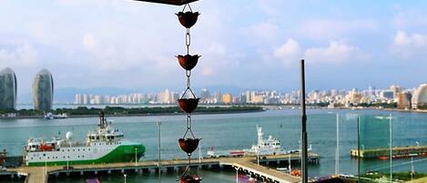 A wooden deck with a bench, a hanging light fixture, and a view of a marina with boats and a city skyline in the background.