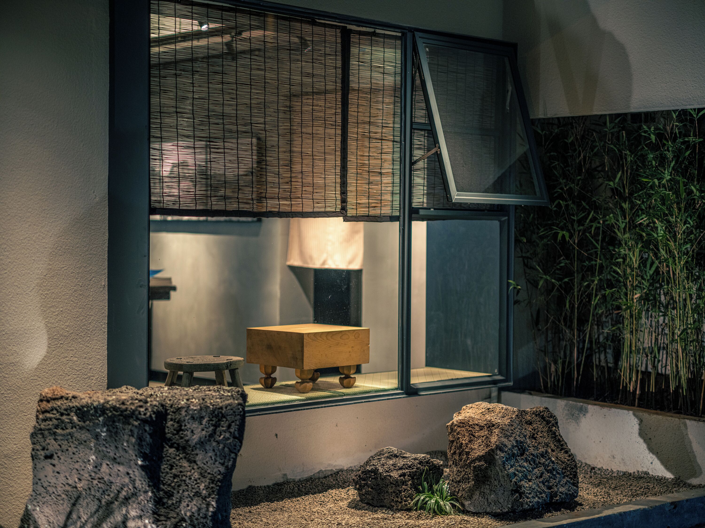 A room with a large window, a wooden stool, and a small table.
