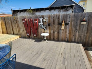 A wooden deck with a metal table and chairs, a wooden fence with painted letters, and a small sign. - 3-bedroom home in Wildwood with AC, WiFi, off street parking, 3blks from beach. (Wildwood)