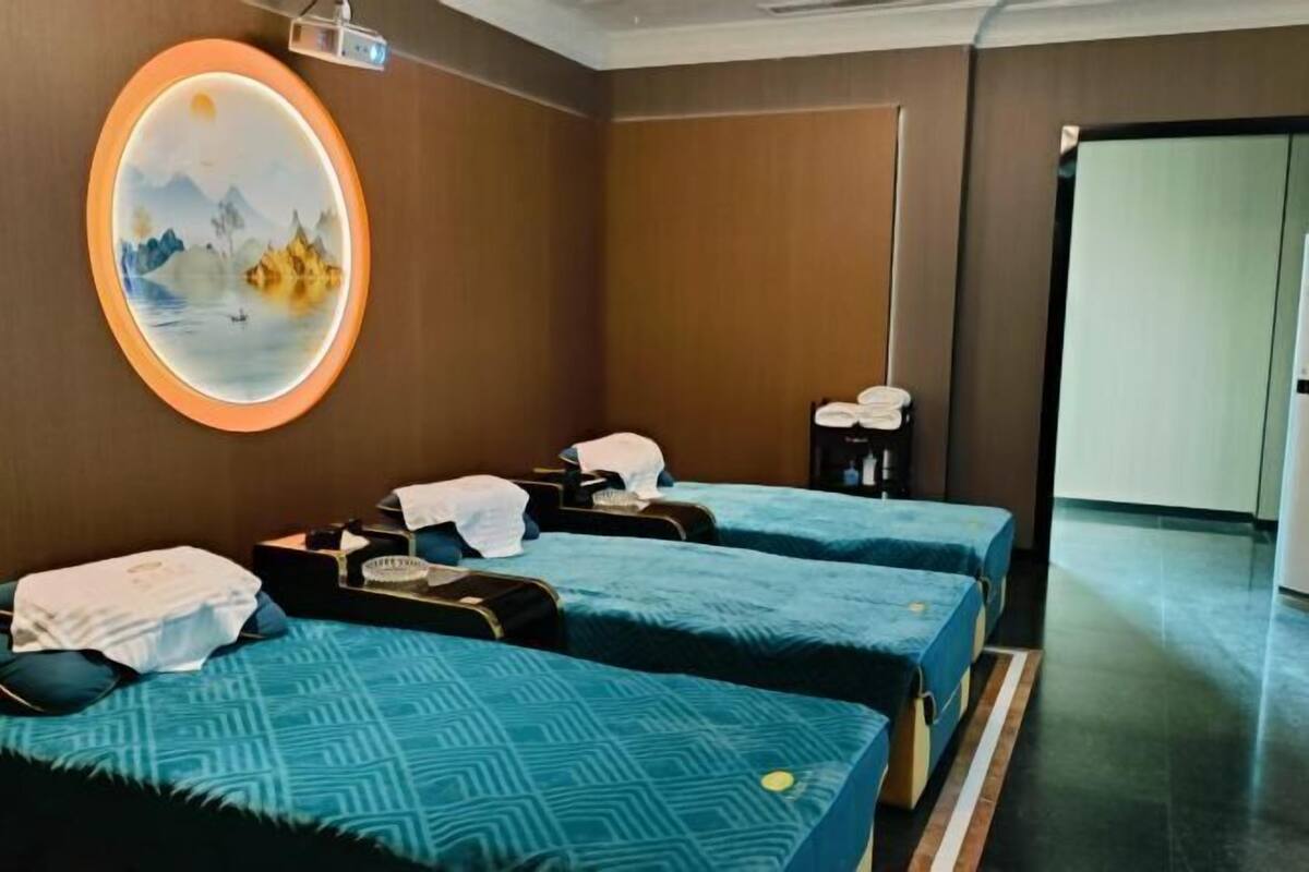 Habitación de hotel con tres camas, un cuadro en la pared, un proyector y una puerta que da a otra habitación.