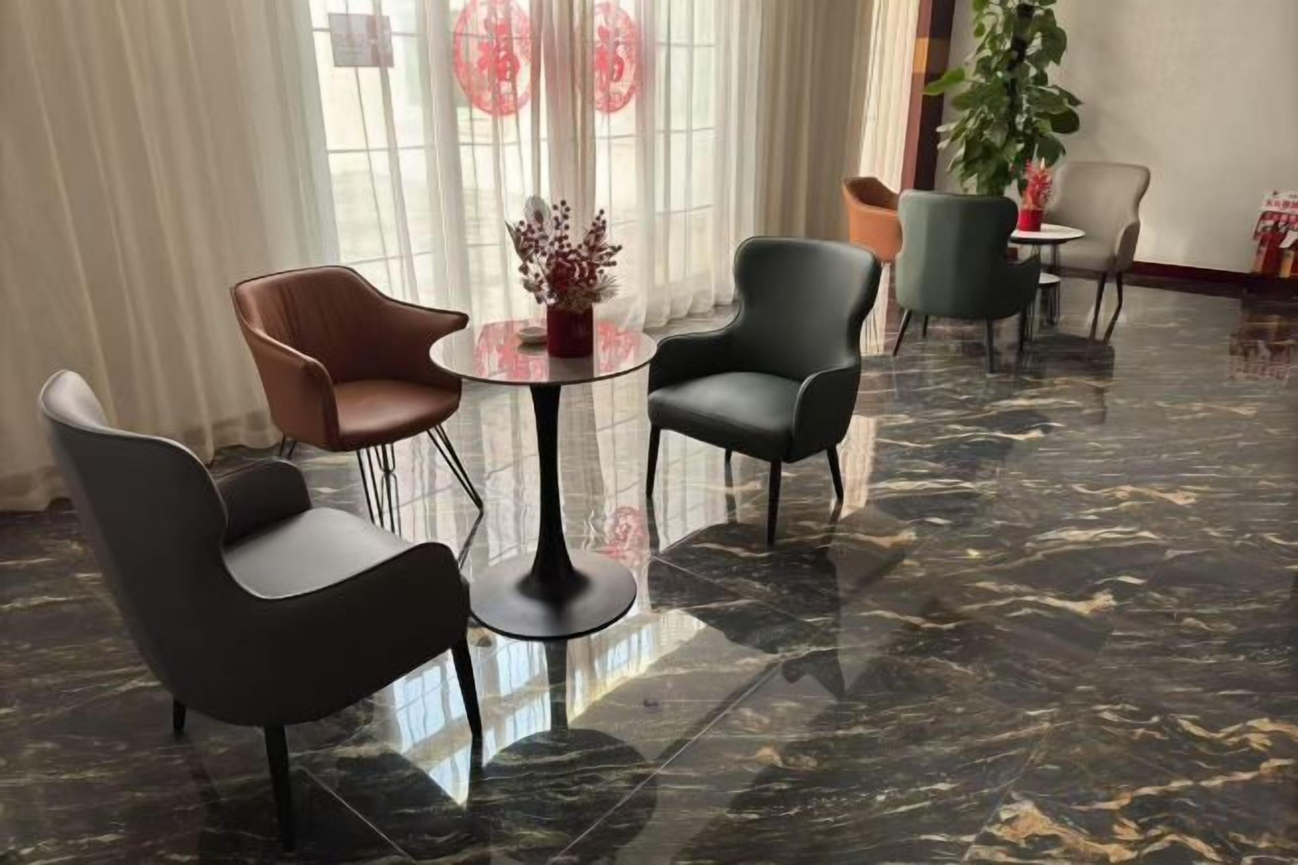 Un hall de hotel con piso de mármol, una mesa redonda con sillas y una planta grande en maceta.
