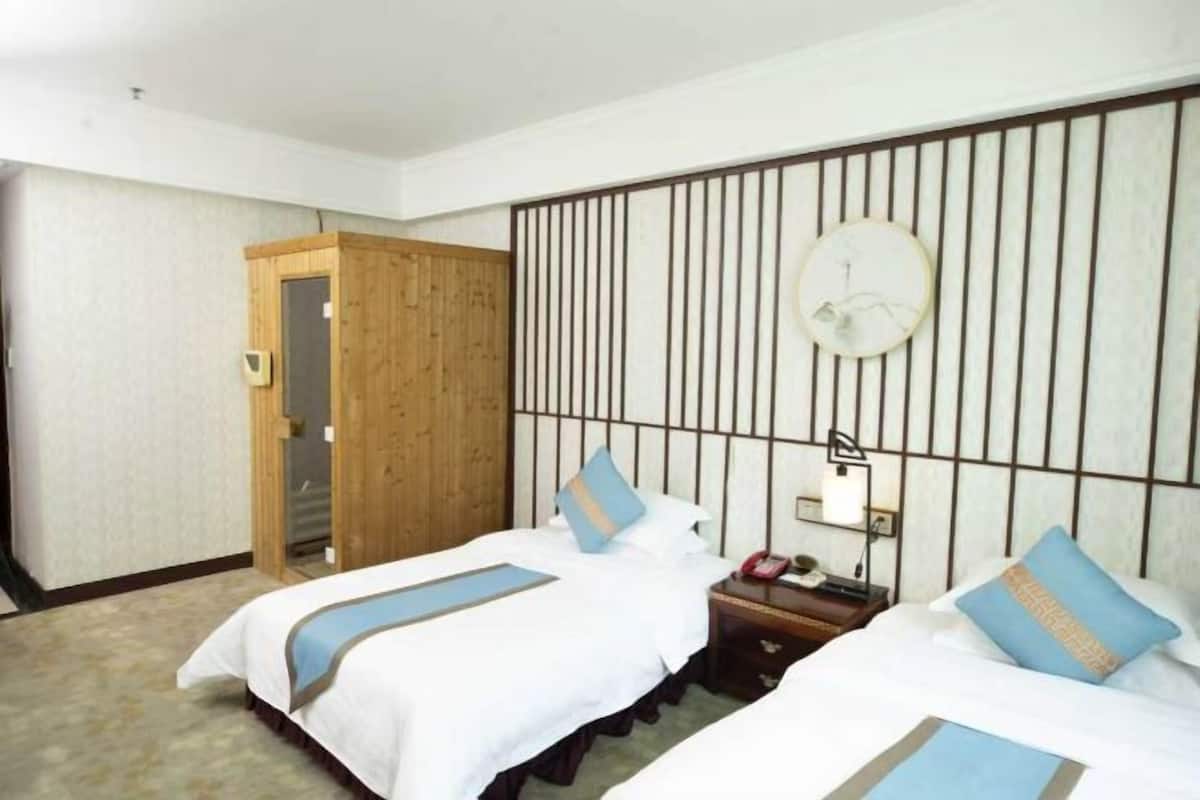 Habitación de hotel con dos camas, un armario de madera, una mesita de noche con lámpara y un reloj de pared.