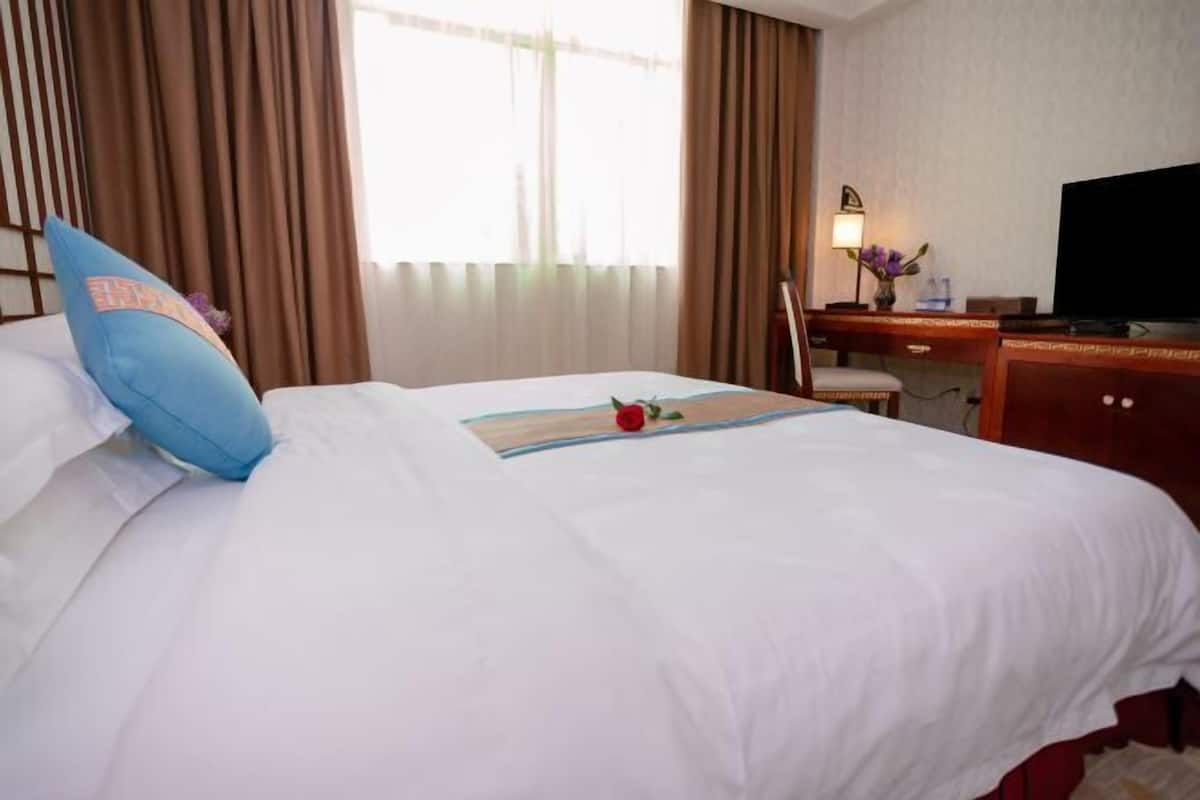 Una habitación de hotel con cama, escritorio con televisor y ventana con cortinas.