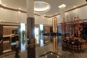 A spacious lobby with a polished floor, a reception desk, and a decorative plant arrangement. - Kaiyue Hotel (Shaoguan)