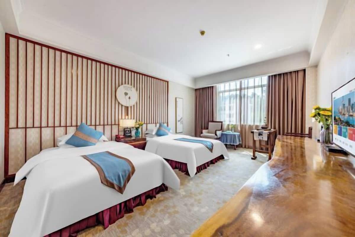 Una habitación de hotel con dos camas, piso de madera, un ventanal grande y un televisor de pantalla plana.