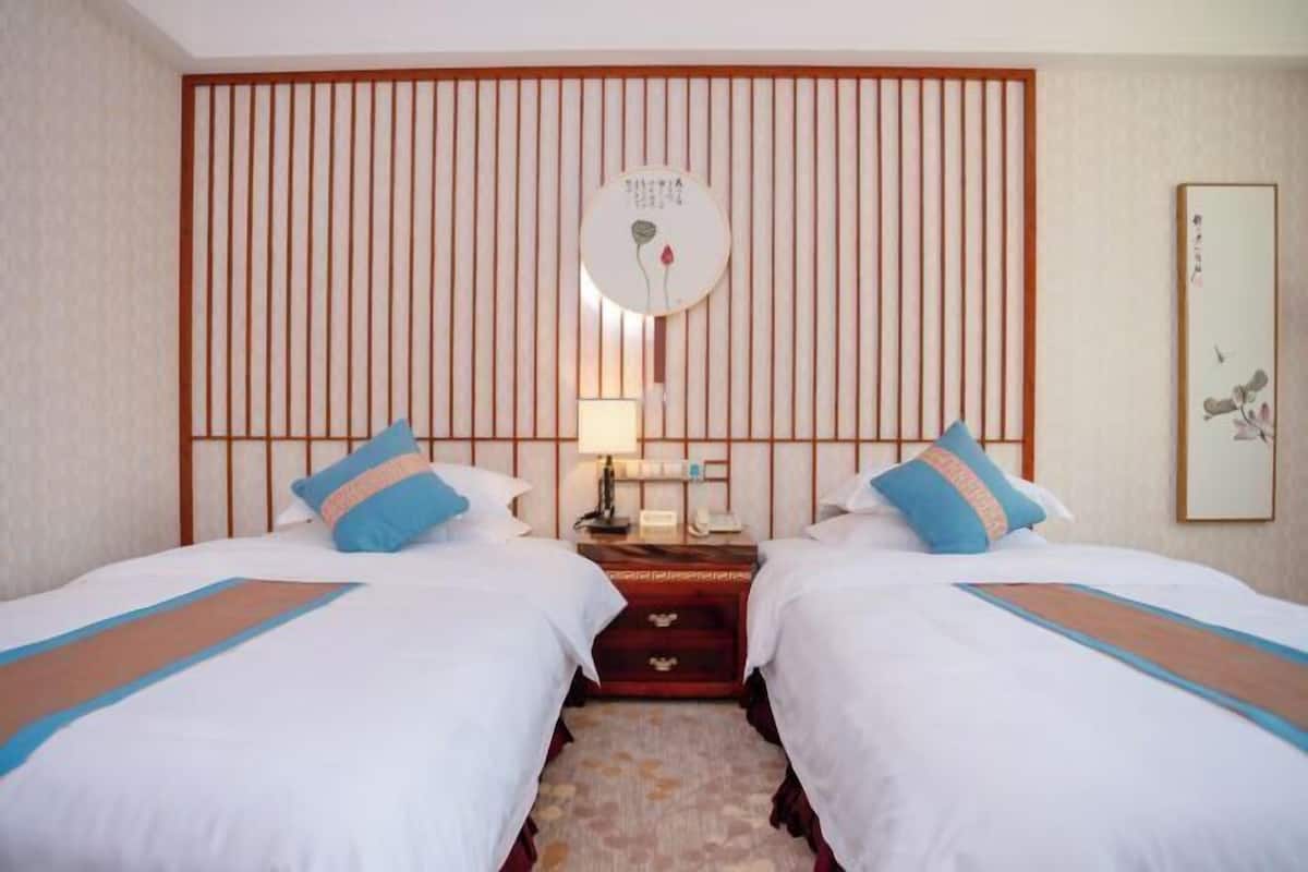 Habitación de hotel con dos camas, cabecera de listones de madera, mesita de noche con lámpara y una obra de arte enmarcada en la pared.