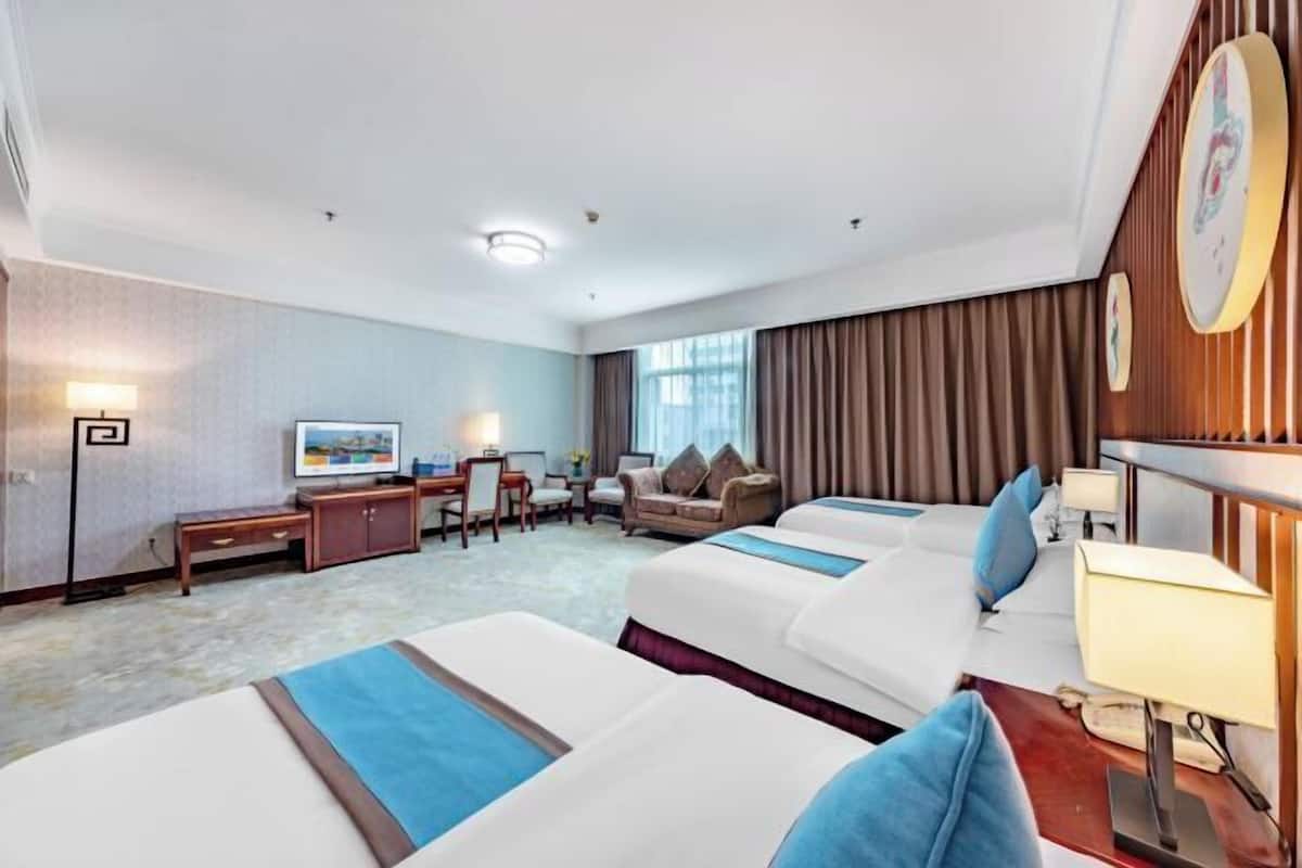 Habitación de hotel con dos camas, un escritorio, una silla, un televisor y una ventana con cortinas.