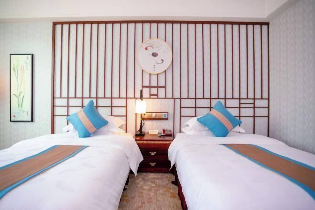 Habitación de hotel con dos camas, una obra de arte colgada en la pared, una mesita de noche y una lámpara.