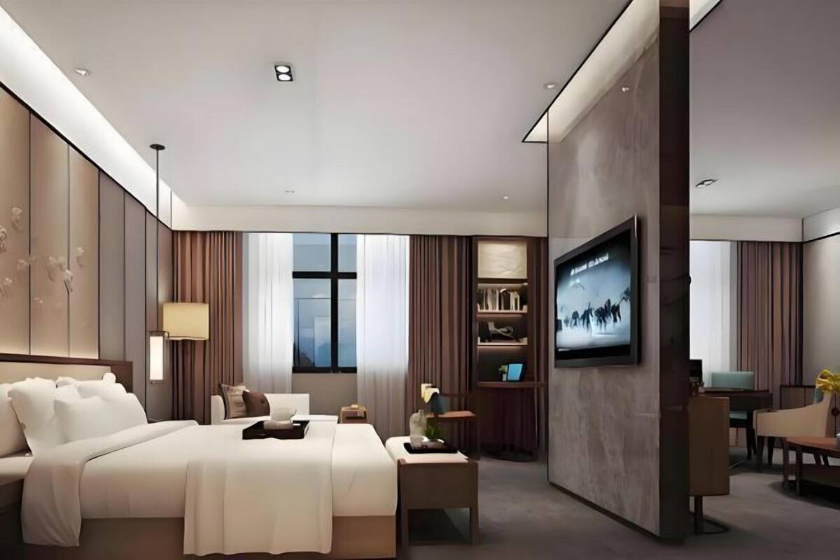 Una habitación de hotel moderna con una cama grande, un televisor montado en la pared, un escritorio y una estantería.