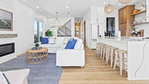 A modern kitchen with white cabinetry, a central island with stools, and pendant lighting. - Luxury 5 BR Beach House - Lagoon View Heated Pool (Gulf Shores)