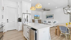 Cocina moderna con armarios blancos, una isla central e iluminación colgante.