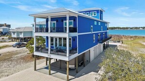 Una casa frente a la playa de dos pisos con balcón, terraza cubierta y vista al agua.