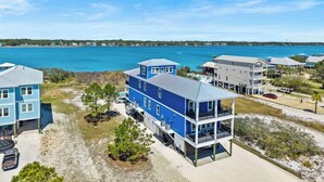 A coastal property with multiple buildings, including a prominent blue structure with balconies and a covered area, adjacent to a sandy beach and a body of water. - Luxury 10 BR Beach House Amazing View Private Pool (Gulf Shores)