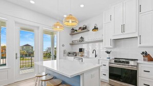 A modern kitchen with white cabinetry, a large island with stools, a built-in oven, and pendant lighting. - Luxury 10 BR Beach House Amazing View Private Pool (Gulf Shores)