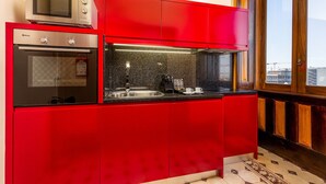 A kitchen with red cabinets, a microwave, an oven, a coffee maker, and a window with a view. - Beach Studio Nearby Market in Oporto (Porto)