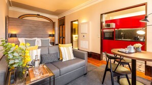 A modern living room with a grey sofa, a coffee table, and a dining area with a red kitchen in the background. - Beach Studio Nearby Market in Oporto (Porto)