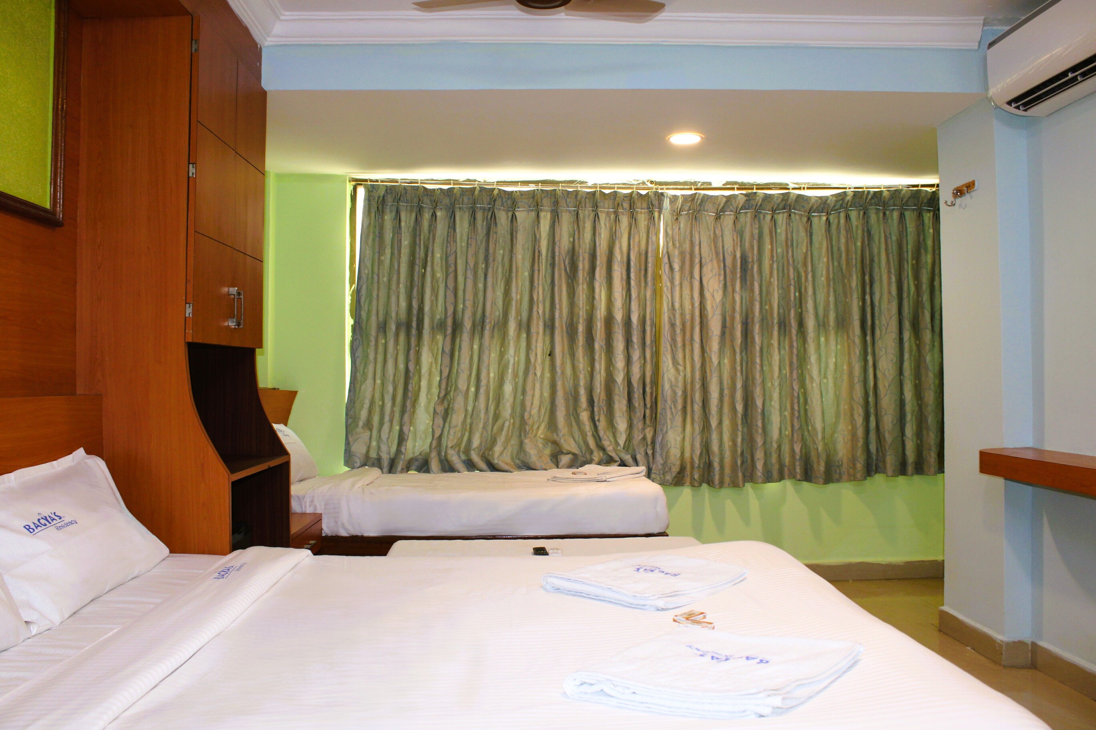 A hotel room with two beds, a wooden wardrobe, a ceiling fan, and a window with curtains.
