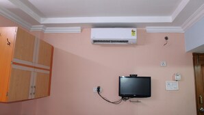Une pièce dotée d’un climatiseur fixé au plafond, d’un téléviseur mural et d’une armoire en bois.
