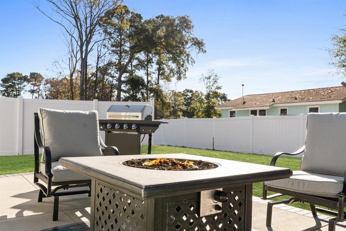 An outdoor patio with a fire pit, two chairs, and a grill.