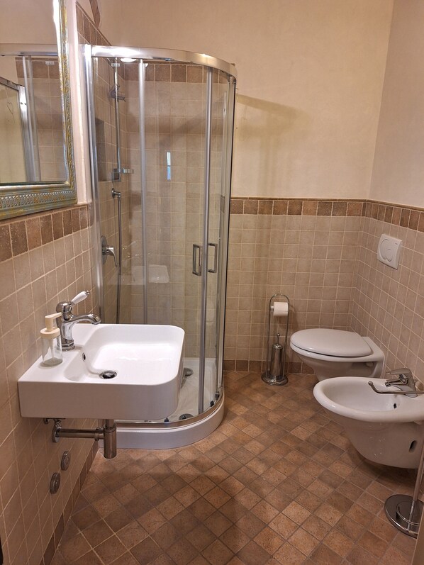 A bathroom with a glass-enclosed shower, a sink, a toilet, and a bidet.