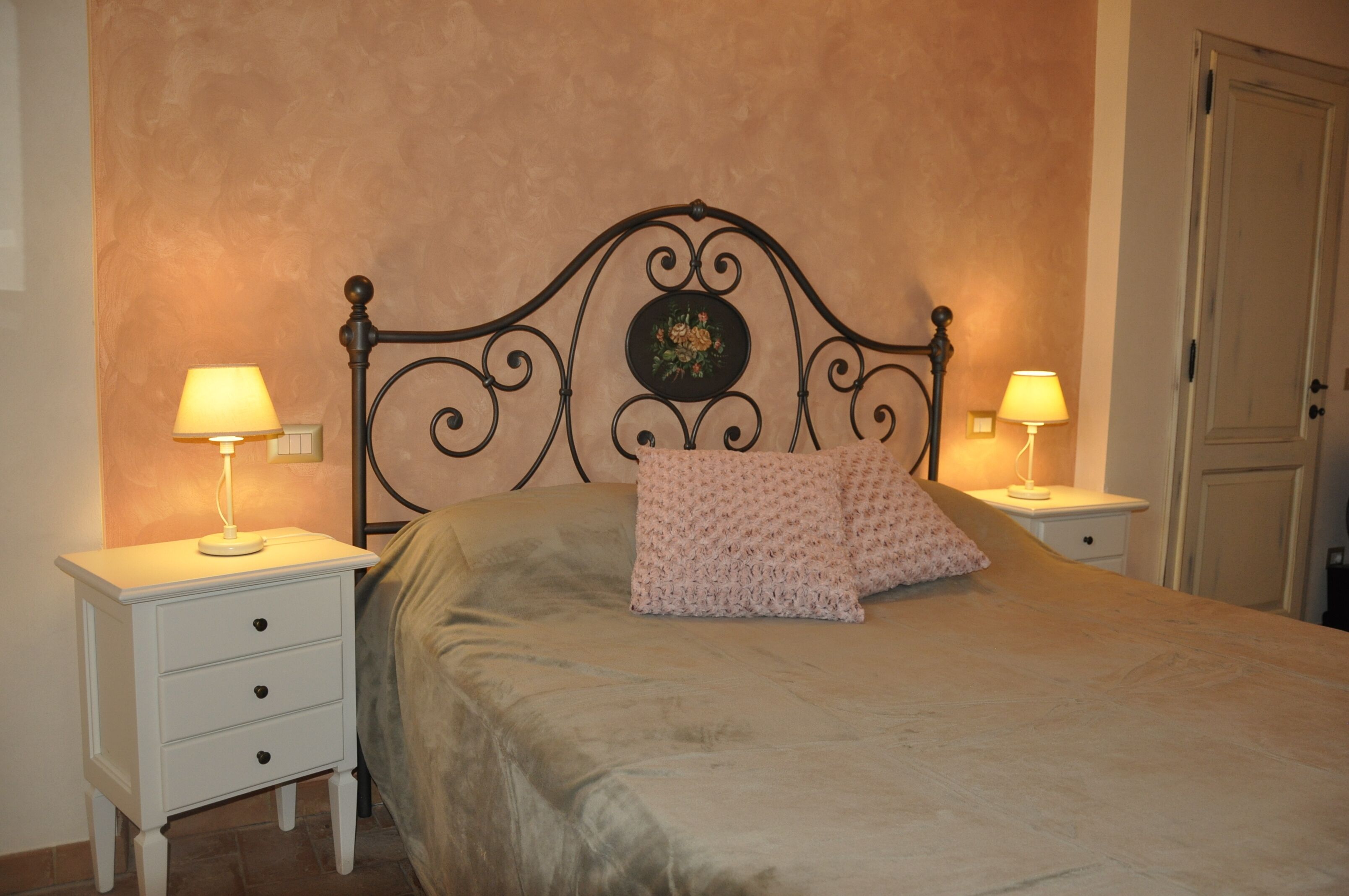 A bedroom with a bed, two bedside tables with lamps, a door, and a wall with a floral design.