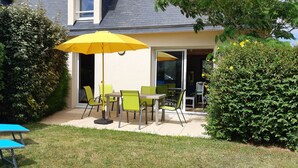 An outdoor patio with a table and chairs, a yellow umbrella, and a blue lounge chair. - Gite Camélias 700 m from the sea and the beach, 3 stars, Portsall, GR34 (Ploudalmézeau)
