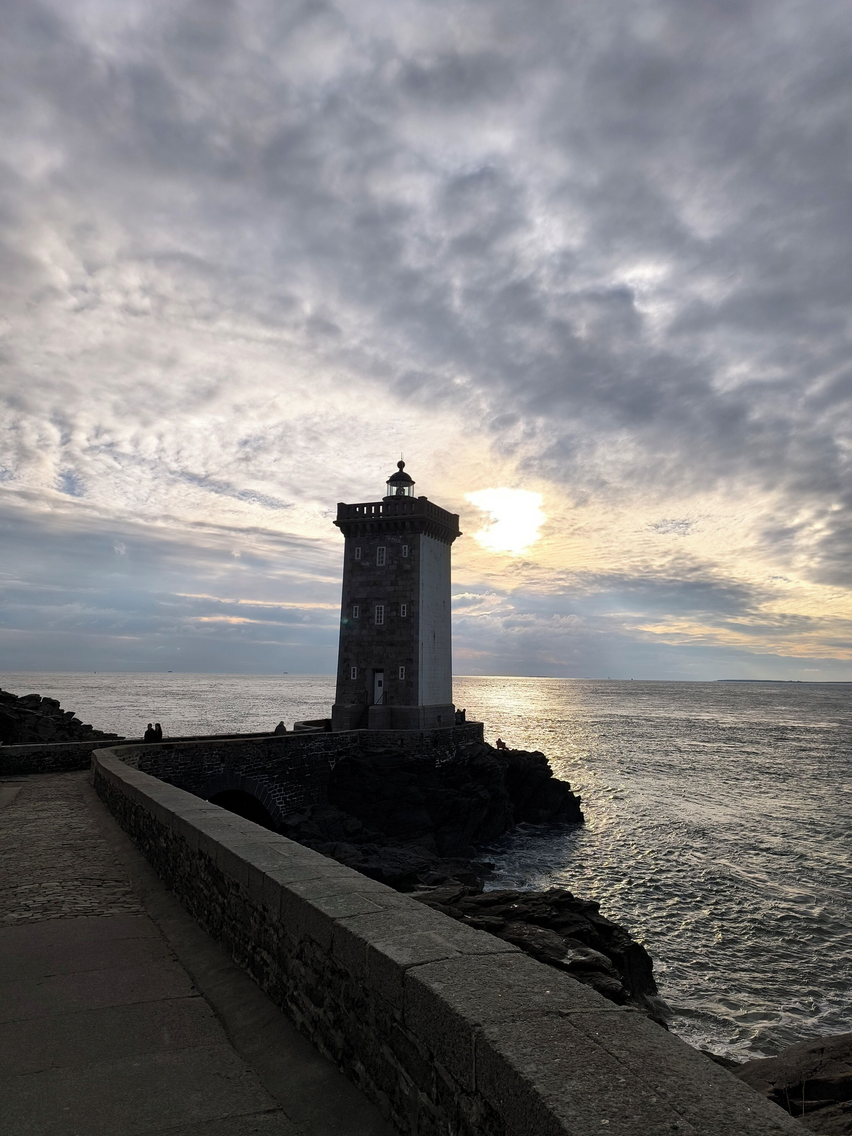 A lighthouse on a rocky coastline with a paved walkway leading to it.