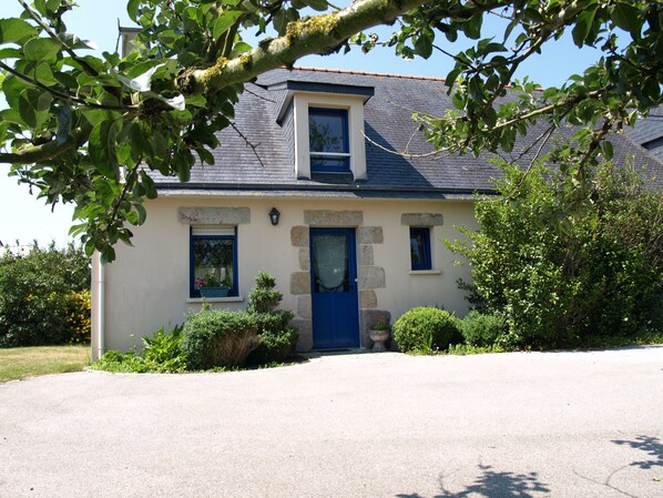 A two-story house with a blue door, a small window, and a stone wall.