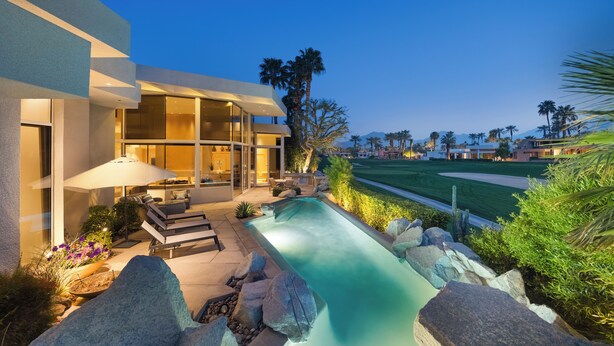 A modern house with a swimming pool, outdoor seating, and a view of a golf course.