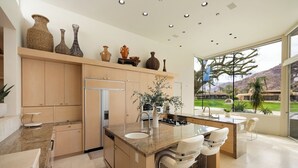 A modern kitchen with a central island, built-in appliances, and a large window offering a view of a landscaped area.