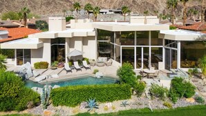 A modern house with a pool, surrounded by palm trees and mountains.