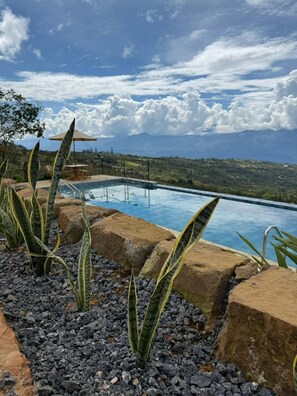 An infinity pool with a view of distant mountains, surrounded by rocks and plants. - Hotel Cariguá (Barichara)