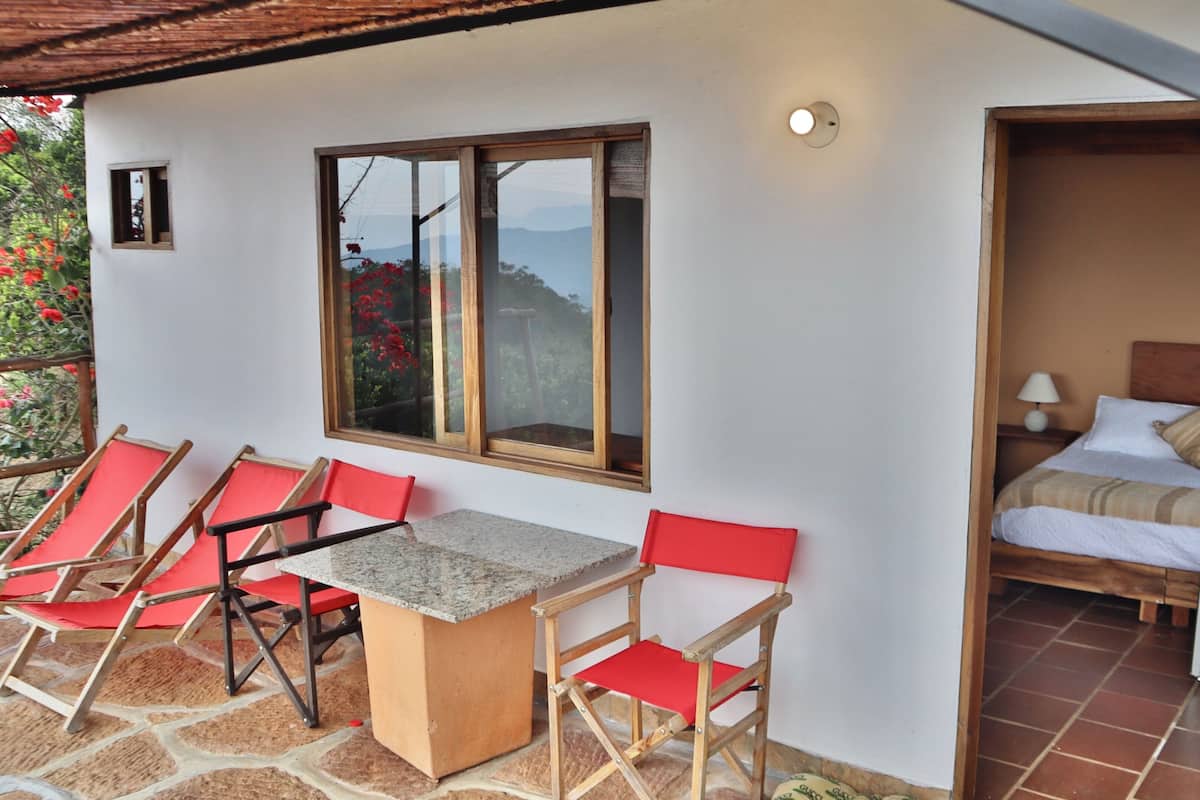 A room with a bed, a small table, and red chairs.
