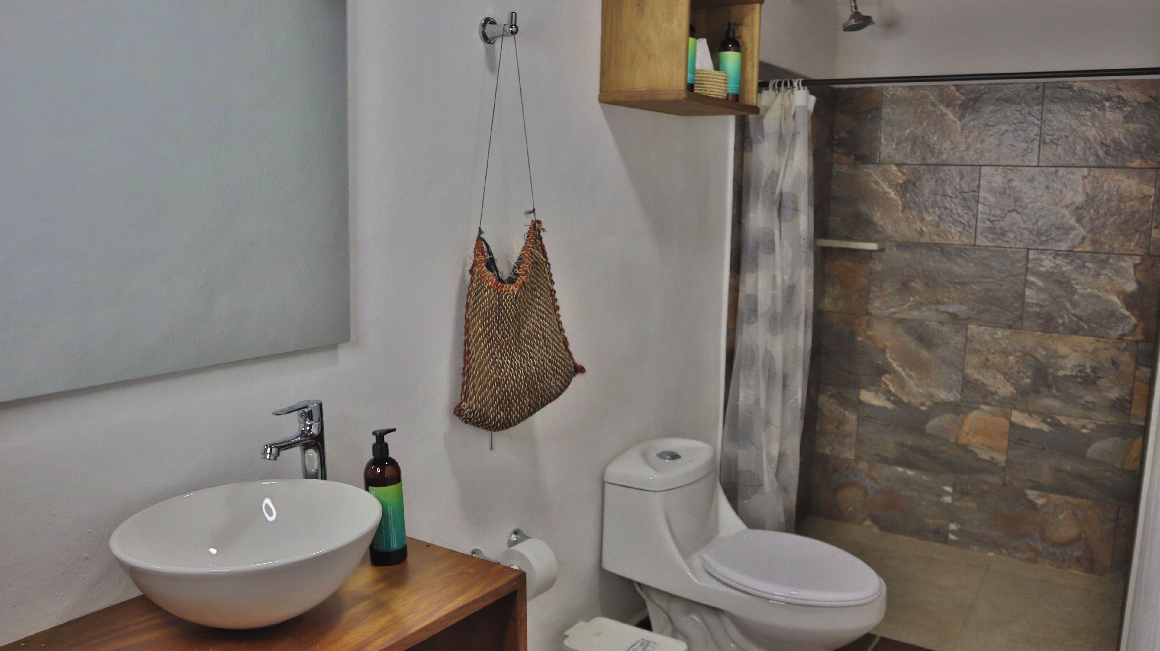 Een badkamer met een wit wastafel, een toilet en een douchegedeelte met stenen tegels.