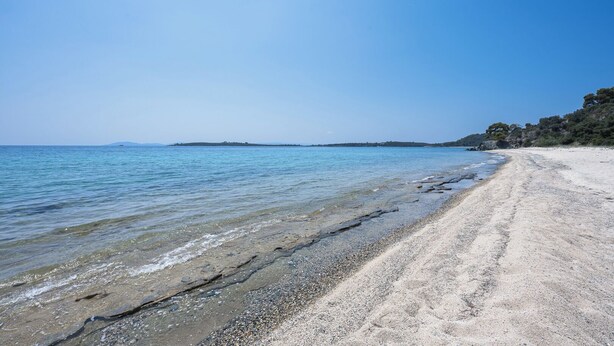 Een strand met helder water, een kiezelstrand en een eiland in de verte.