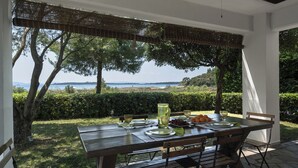 Een terras met eettafel voor twee, met uitzicht op zee en heuvels.